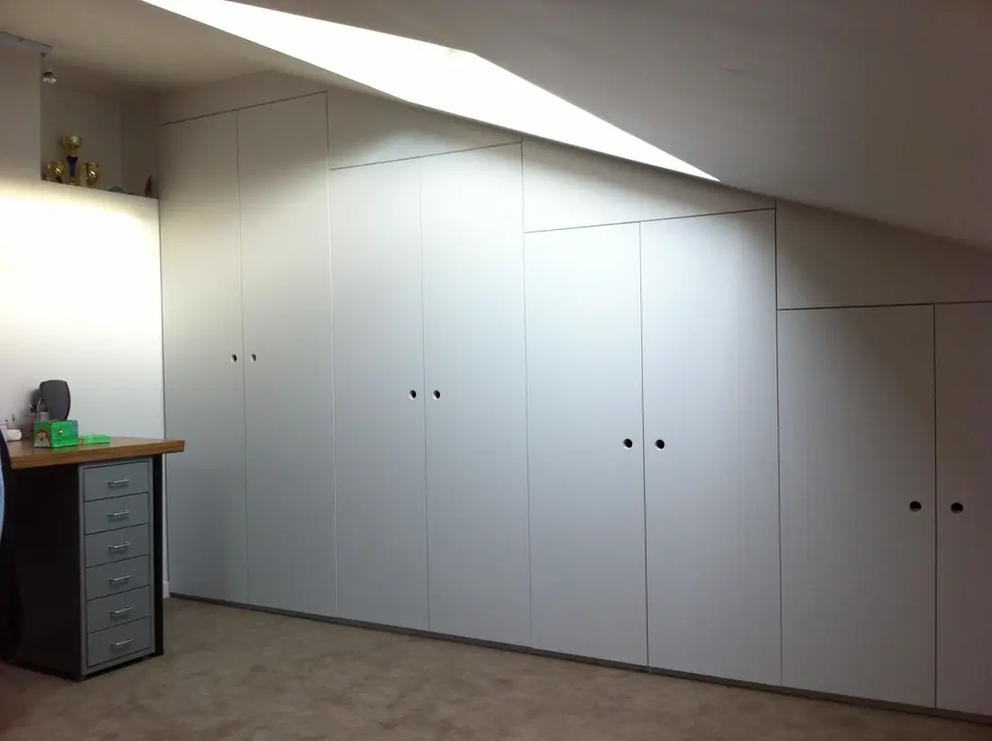 Rangements blancs épousant une sous-pente, avec plan de bureau en retour