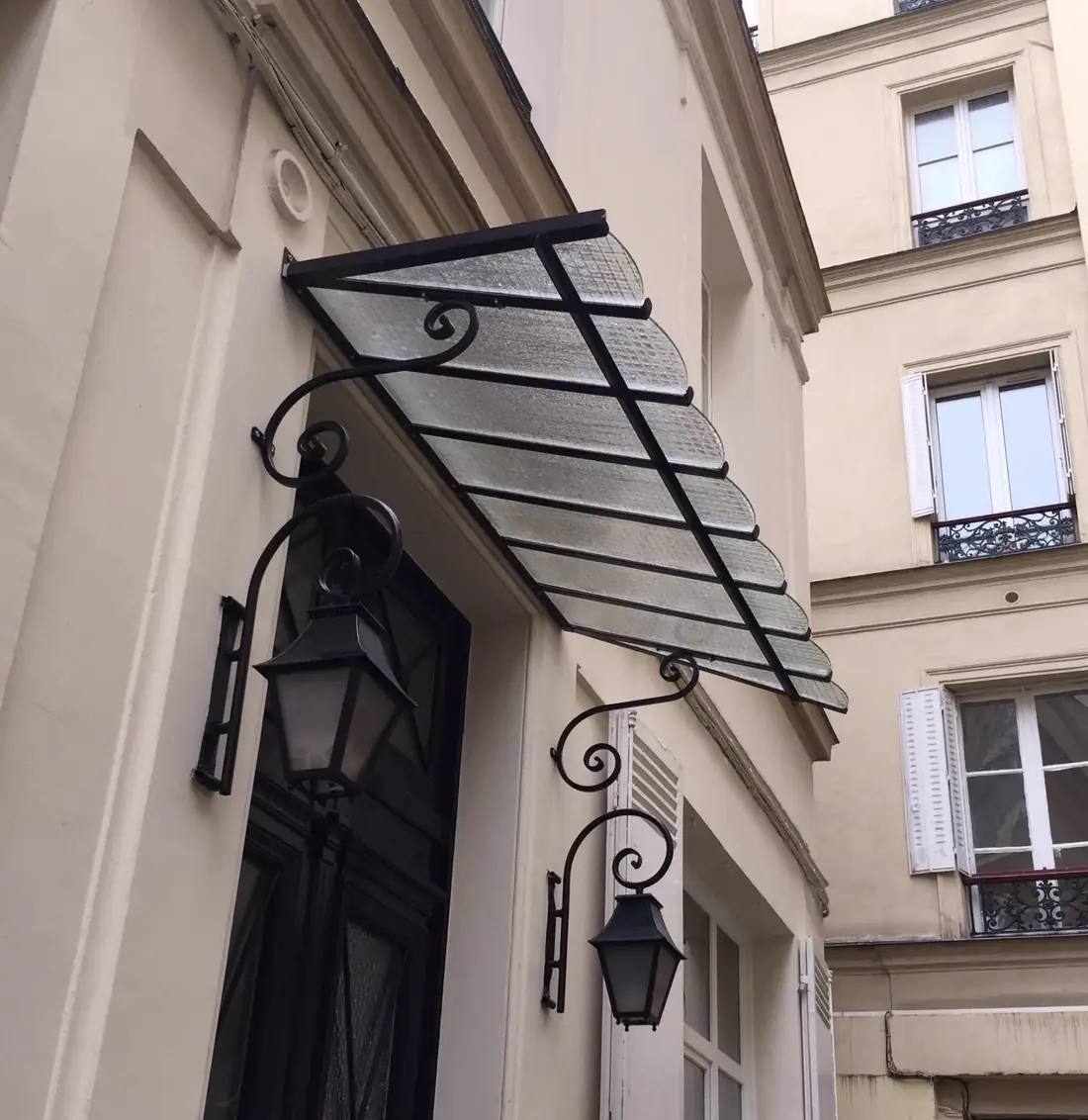 Marquise en acier et verre encadrée de deux lanternes, au-dessus d’une porte d’immeuble