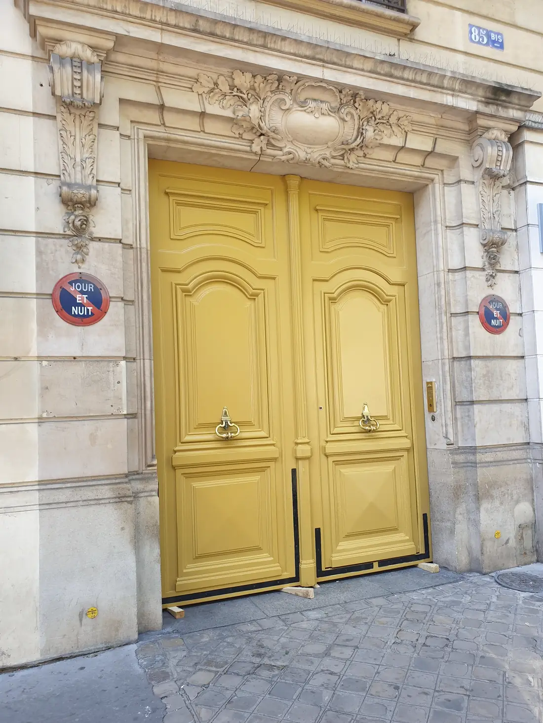 Porte cochère jaune d’un immeuble haussmannien, encadrement de pierre sculpté