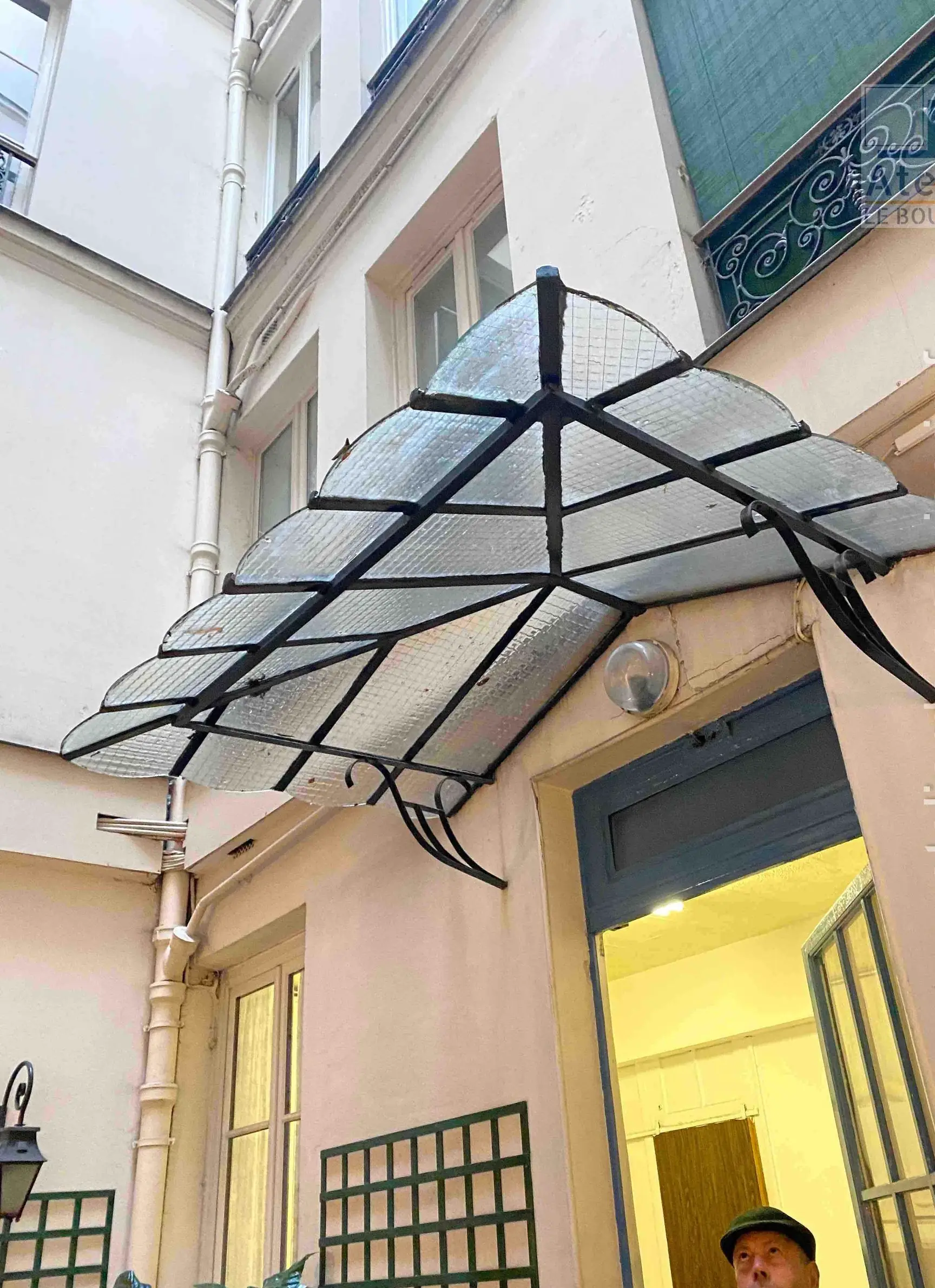 Marquise en acier et verre déployée en éventail au-dessus d’une porte de cour