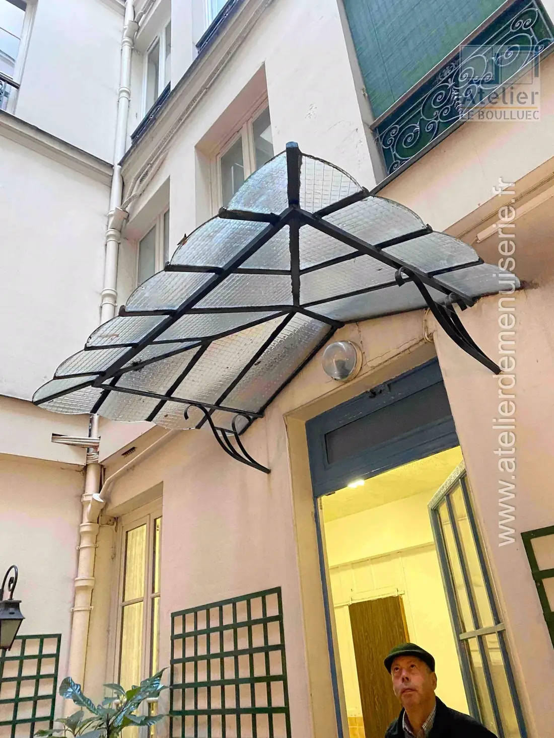 Marquise en acier et verre déployée en éventail au-dessus d’une porte de cour