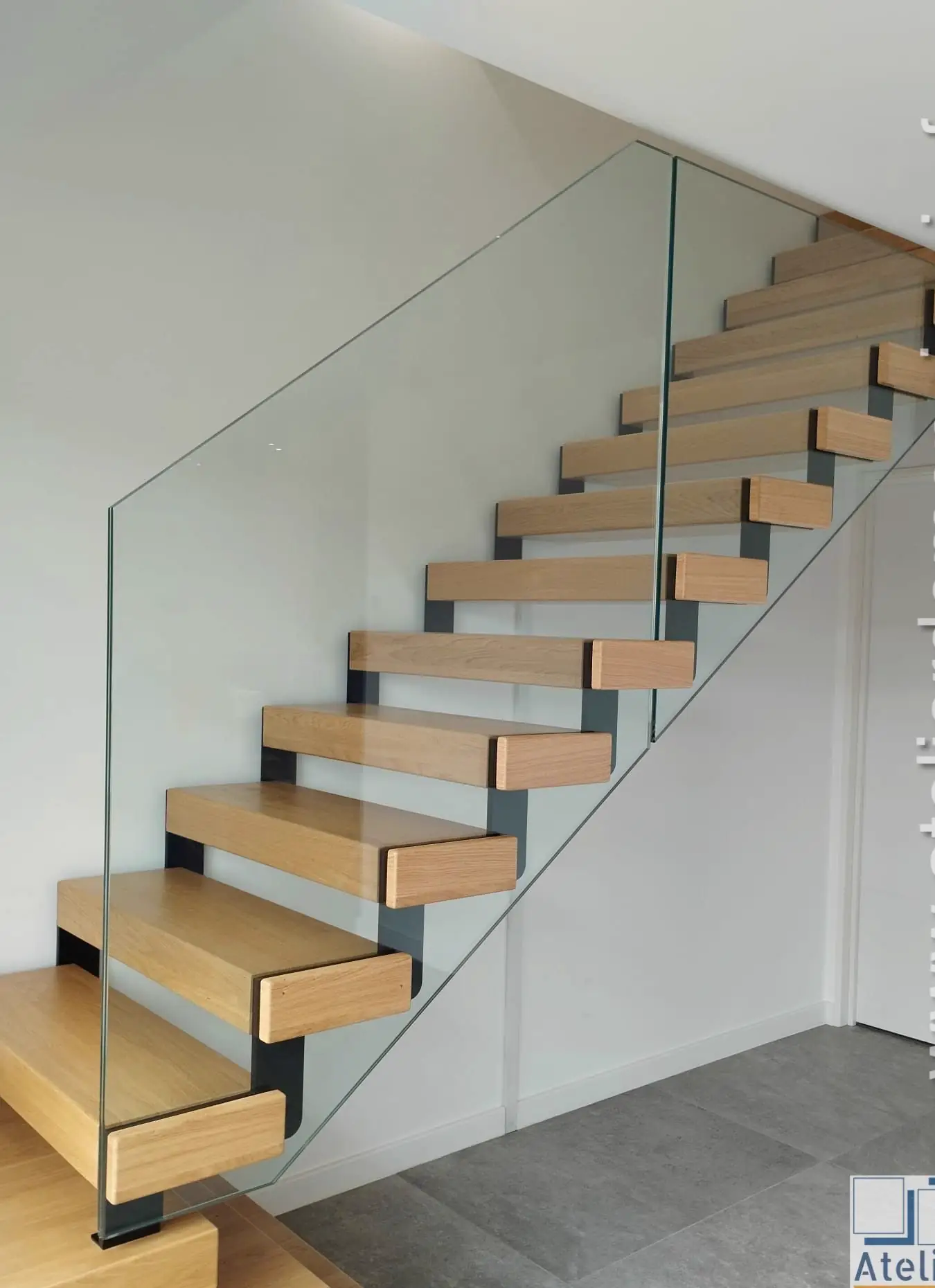Escalier à limon acier noir, marches en bois clair et garde-corps en verre