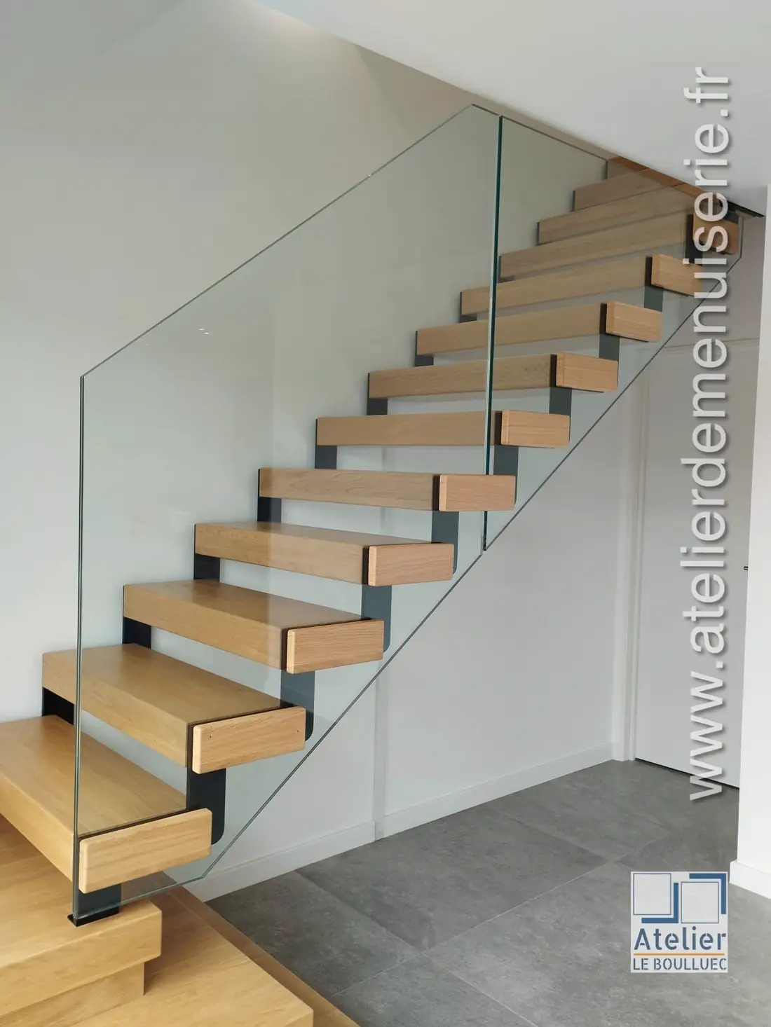 Escalier à limon acier noir, marches en bois clair et garde-corps en verre