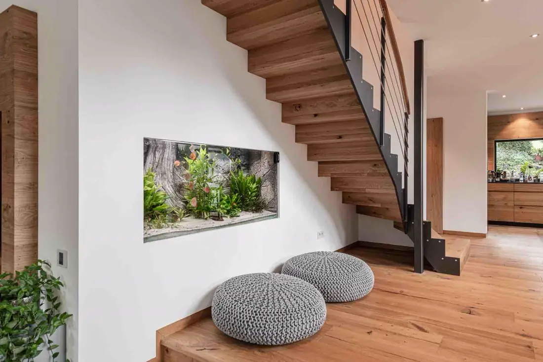 Escalier en bois à limon acier devant un mur habillé de bois, aquarium encastré
