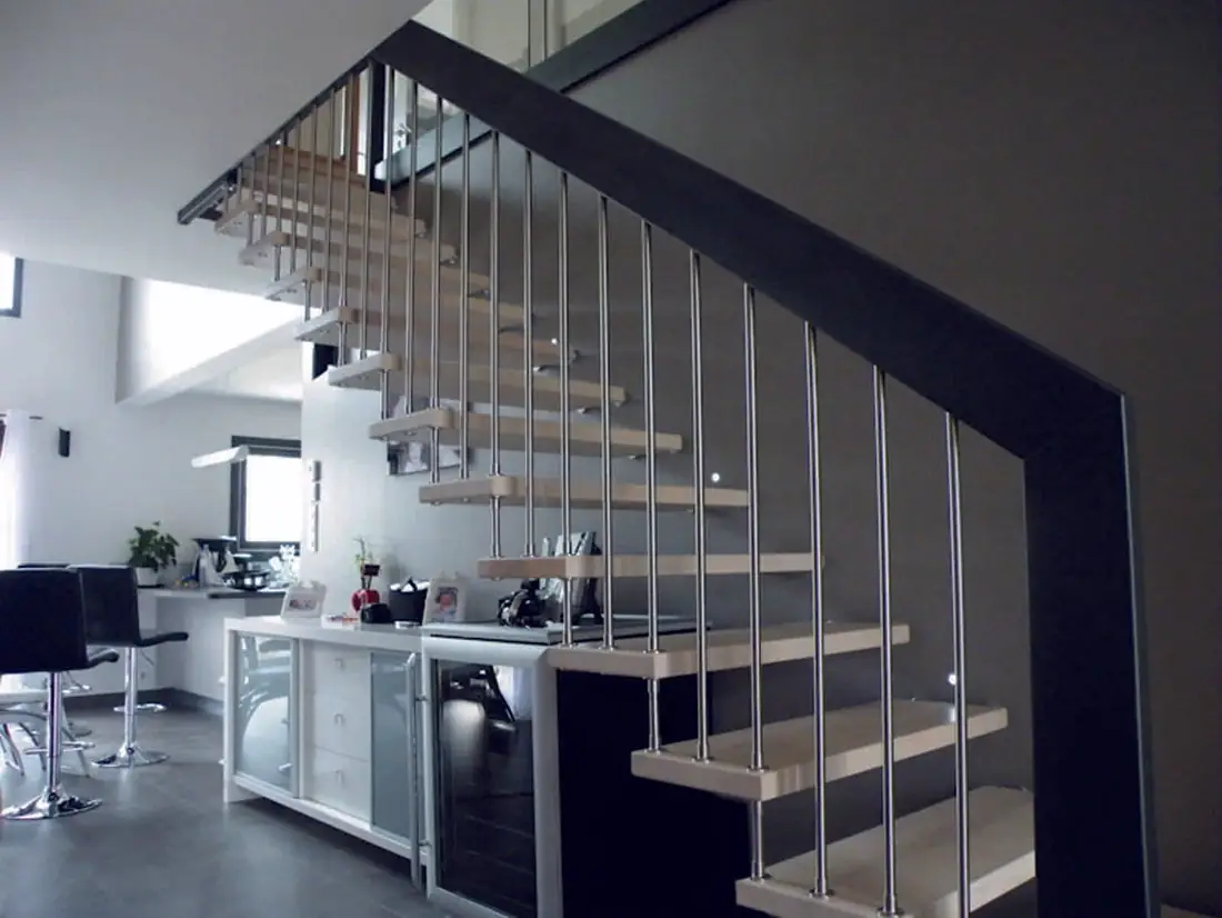 Escalier à marches en bois et balustres inox, vu depuis une cuisine ouverte