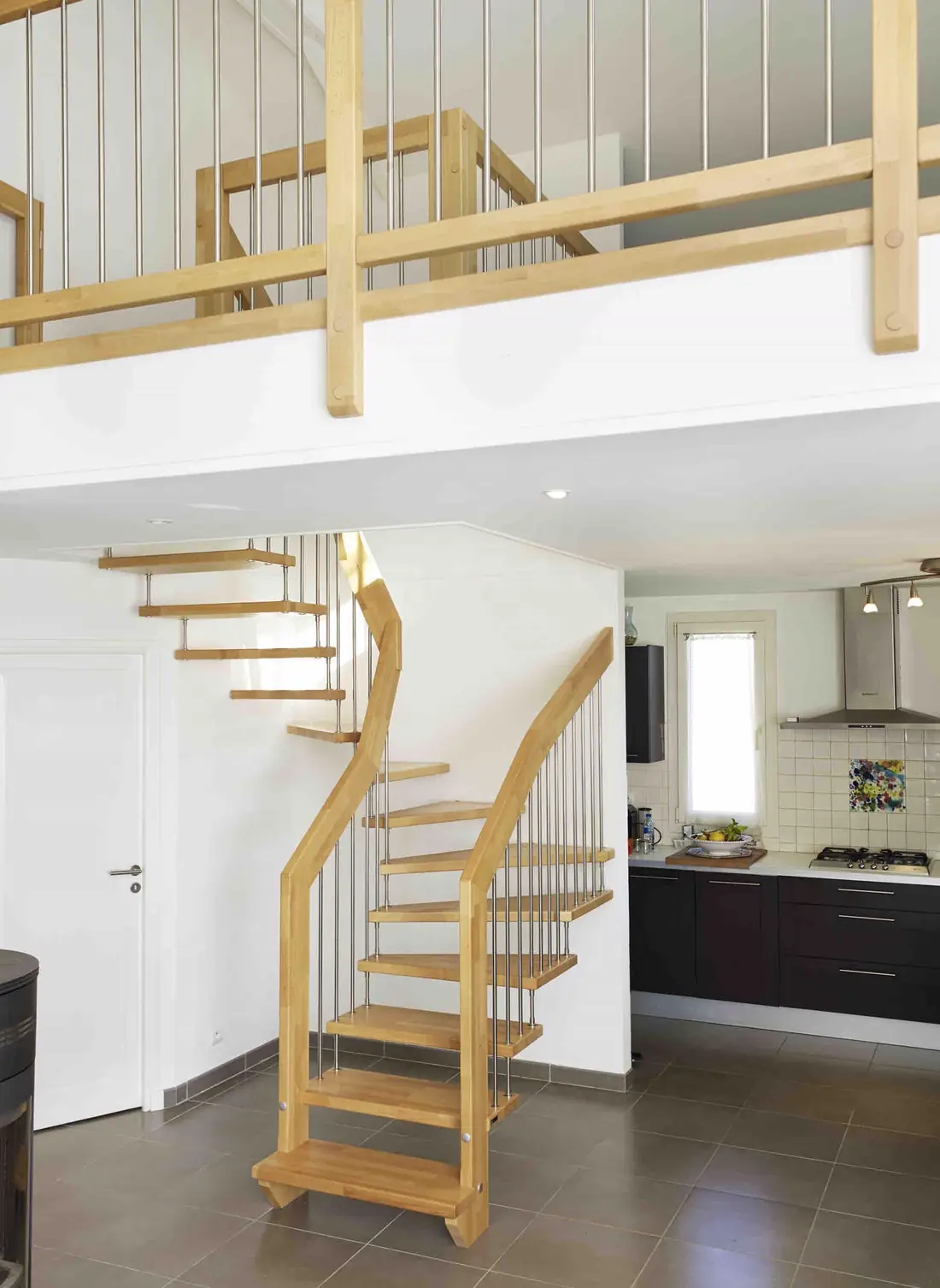 Escalier en bois quart tournant desservant une mezzanine, cuisine au second plan
