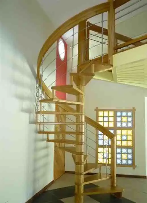 Escalier hélicoïdal en bois à balustres inox, devant une fenêtre à petits carreaux