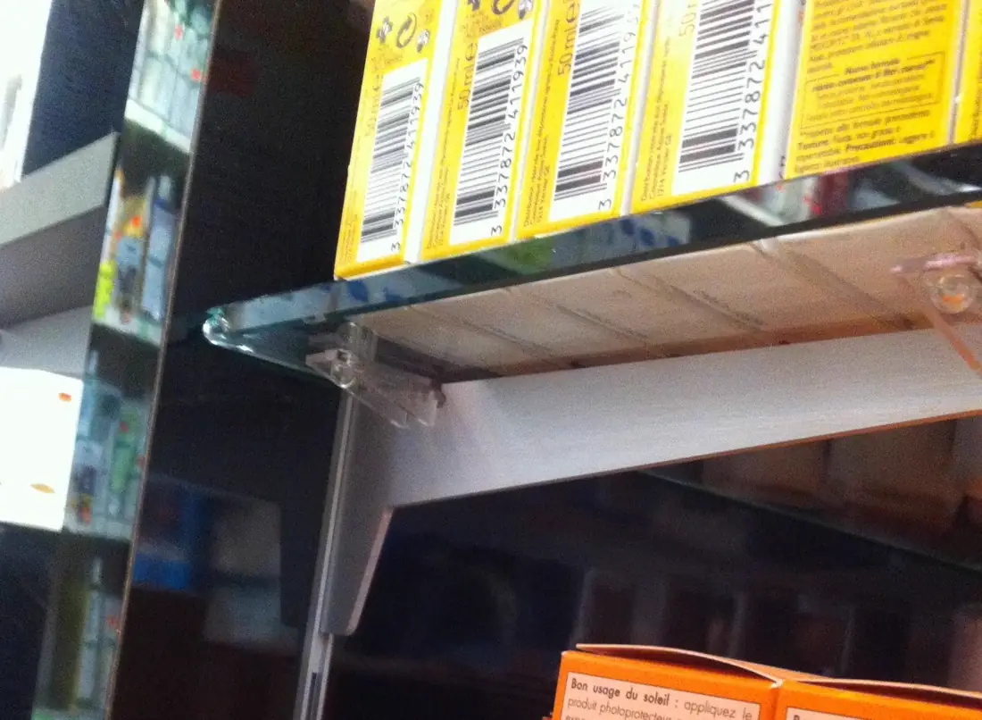 Détail d’une tablette en verre à chants polis fixée sur un présentoir noir