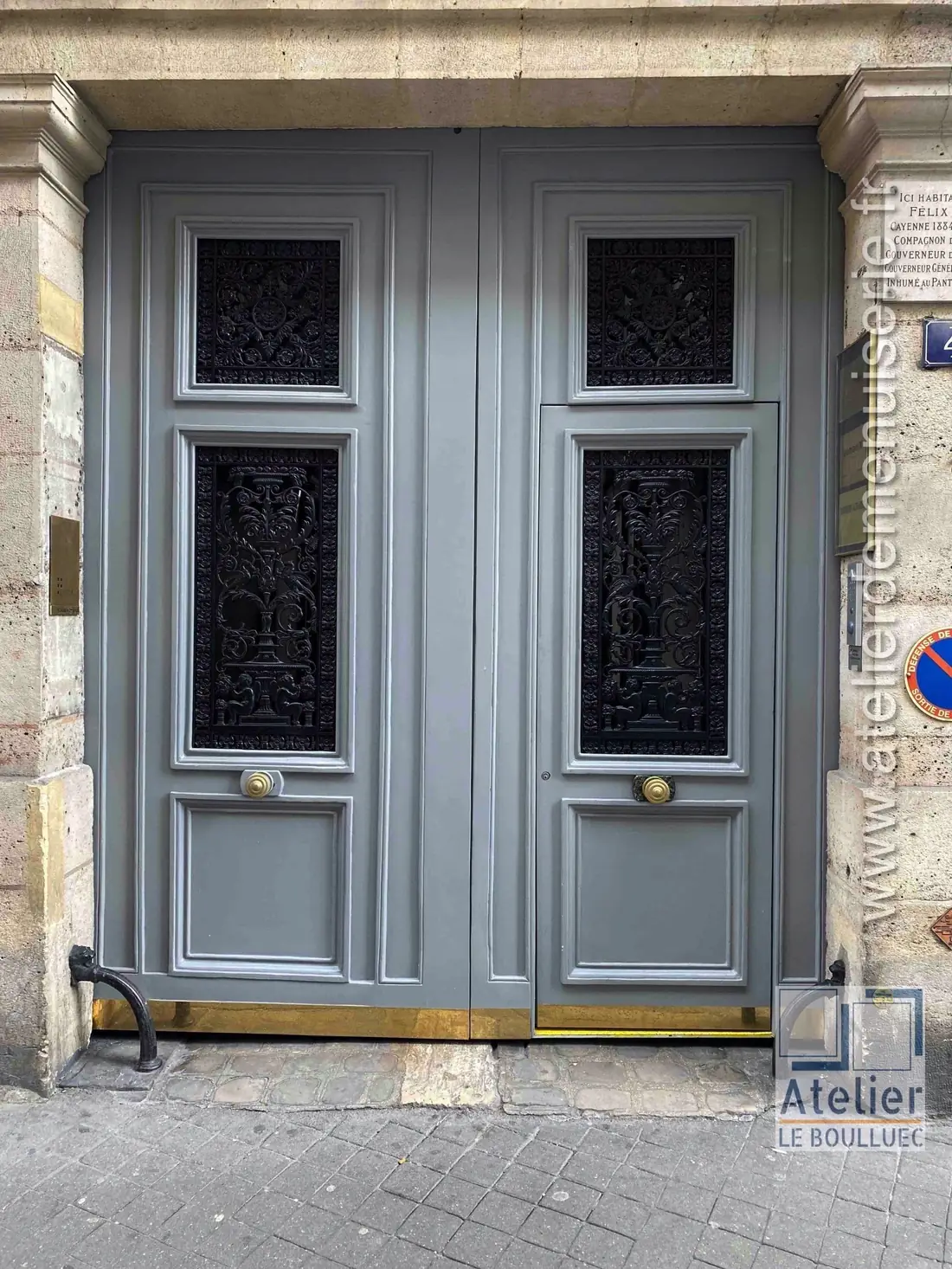 Porte cochère gris-vert à grilles ouvragées, sous une imposte en demi-lune
