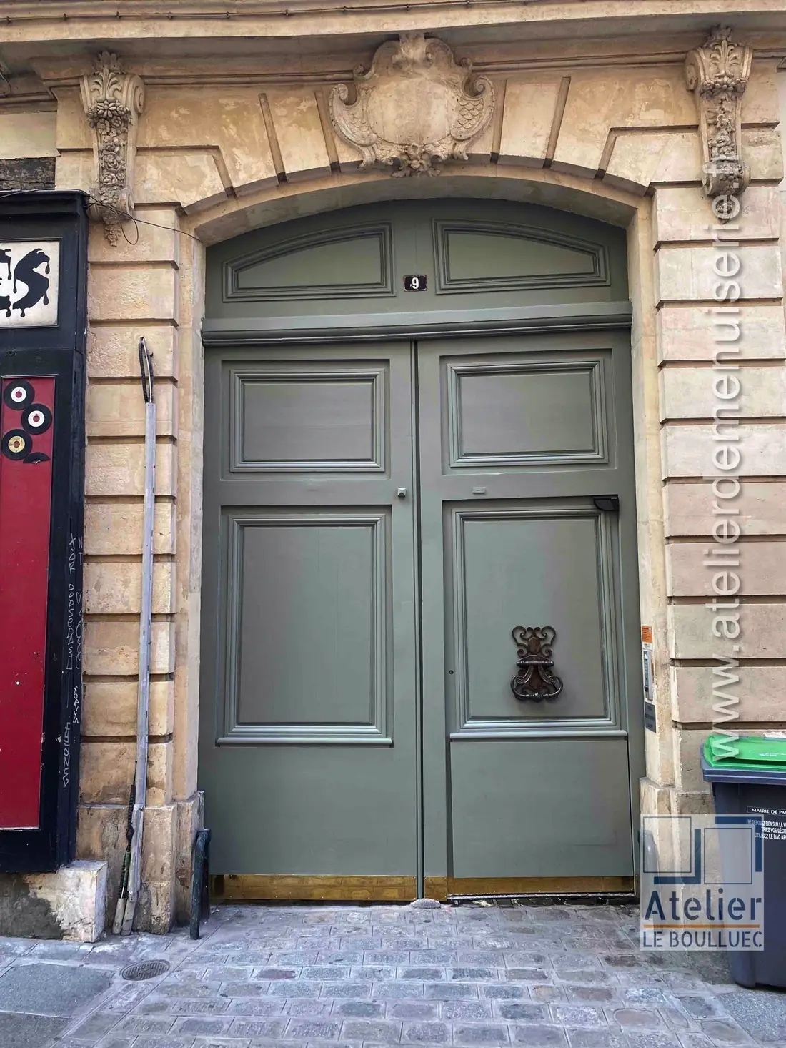 Porte cochère vert olive à heurtoir, sous un encadrement de pierre sculpté