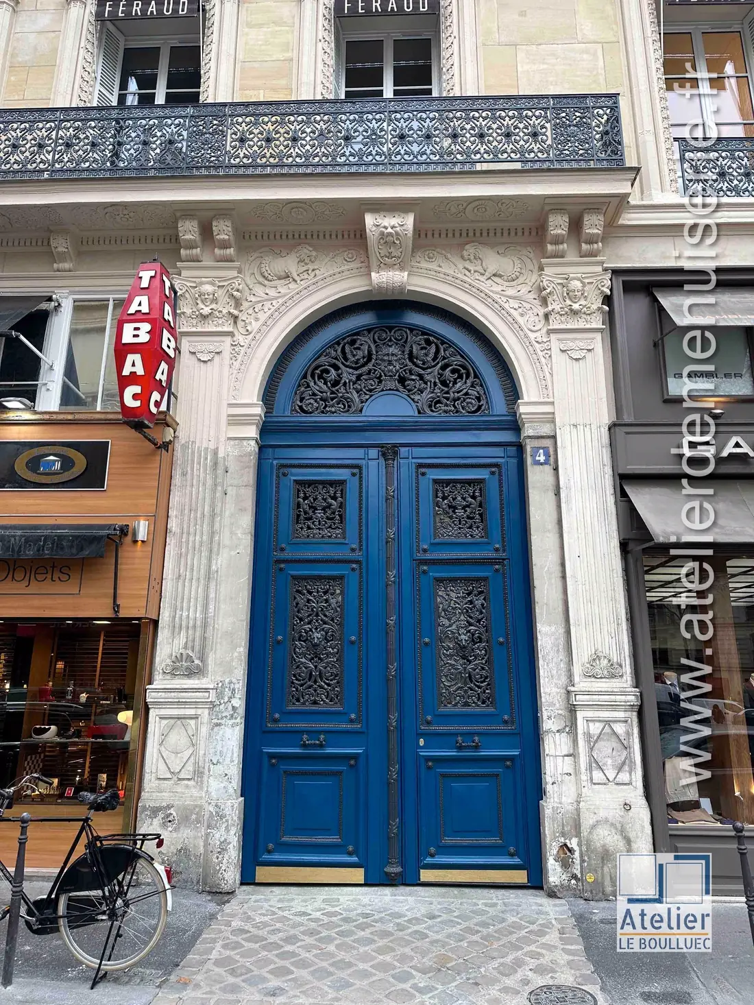 Porte cochère bleue à panneaux ouvragés, entre deux devantures de commerce