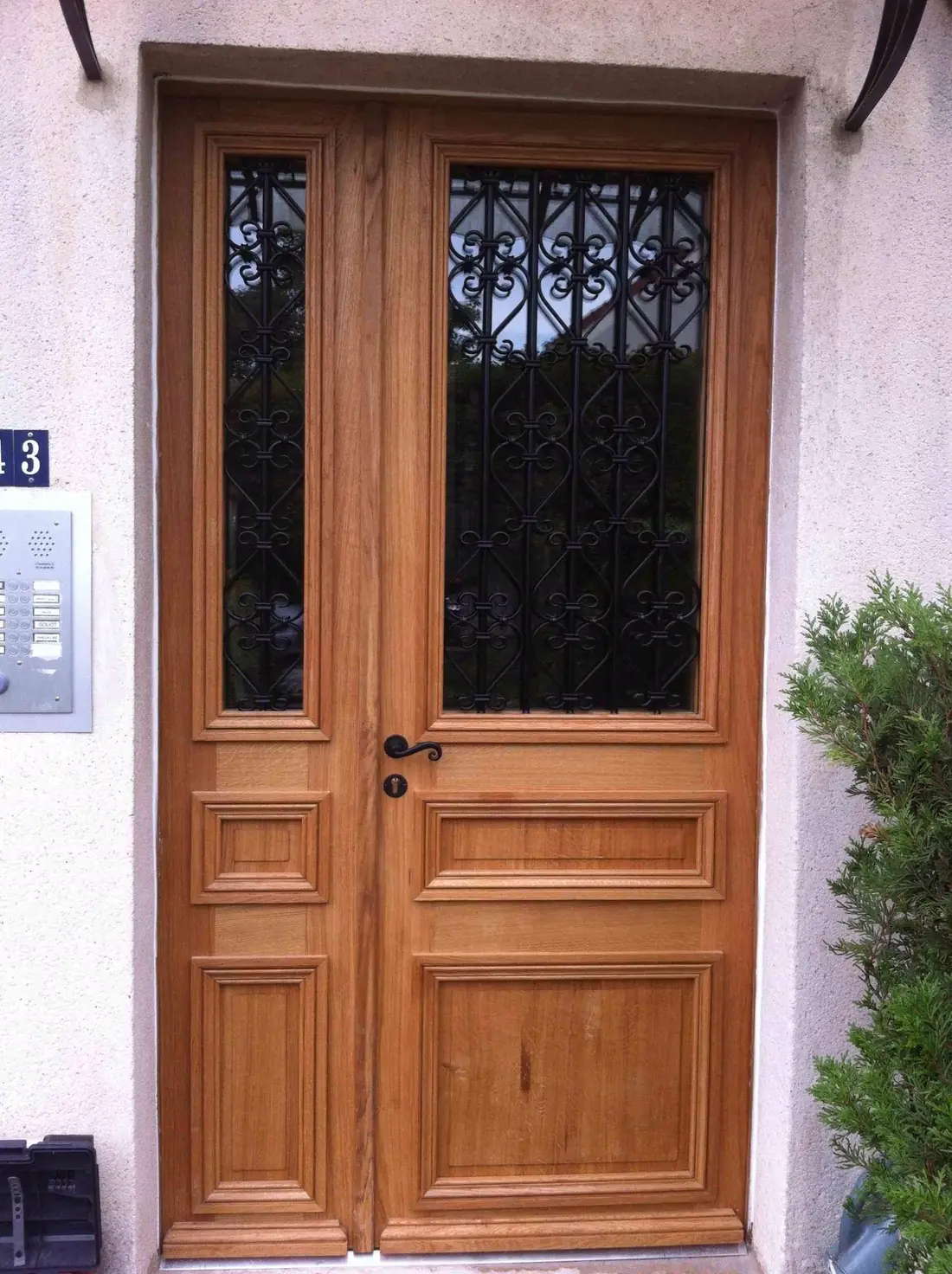 Porte tiercée en chêne clair à grilles ouvragées, sur une façade rose