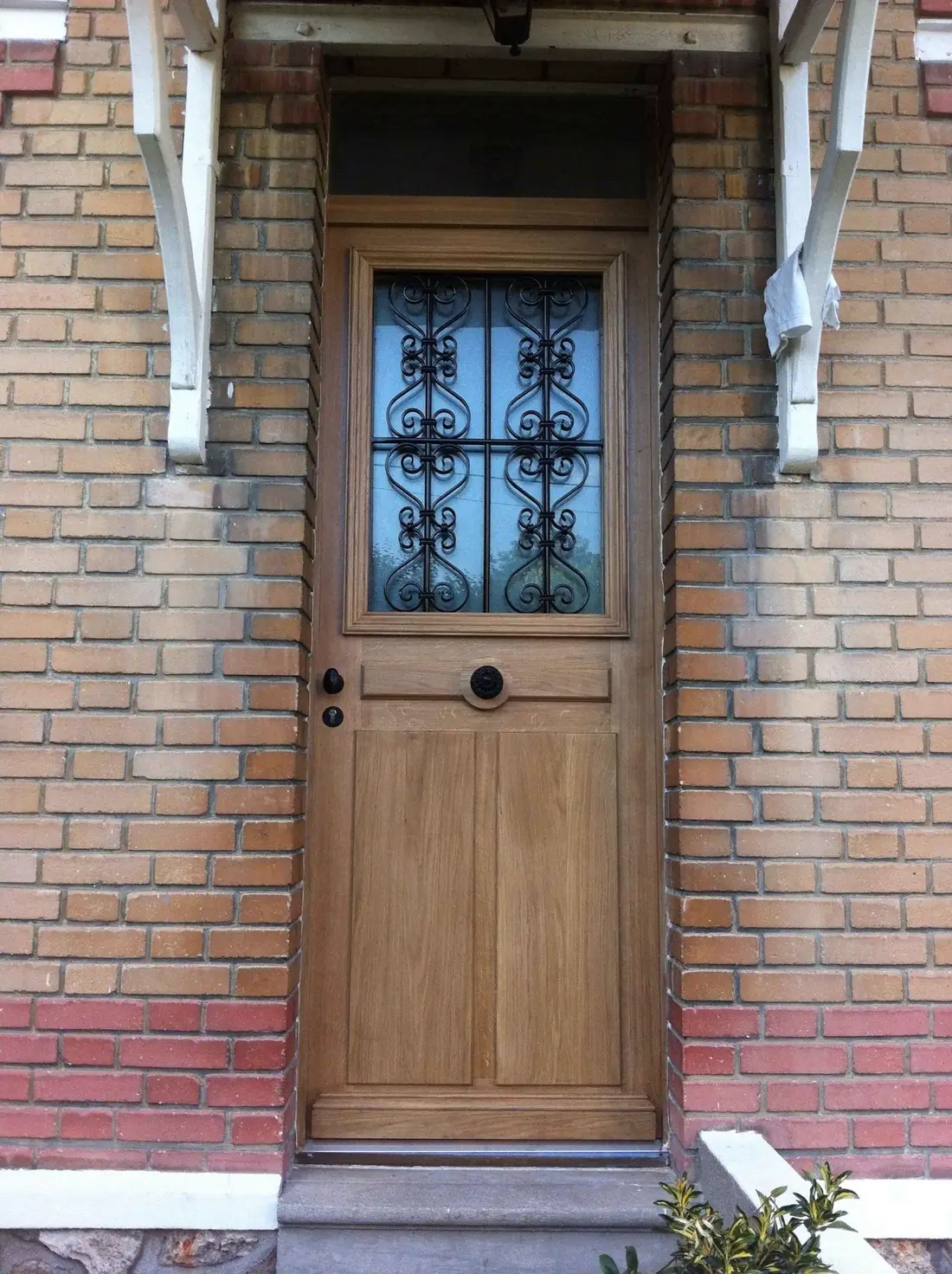 Porte de pavillon en chêne à oculus grillé, sous une marquise, façade de brique