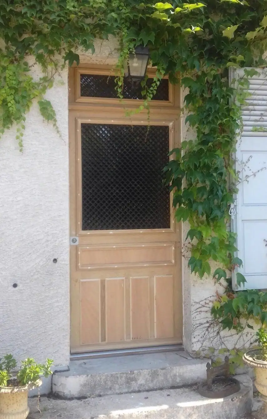 Porte de pavillon en chêne clair à grille losangée, encadrée de vigne