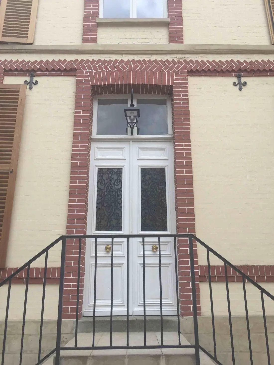 Porte d’entrée blanche à deux vantaux en haut d’un perron, façade de brique
