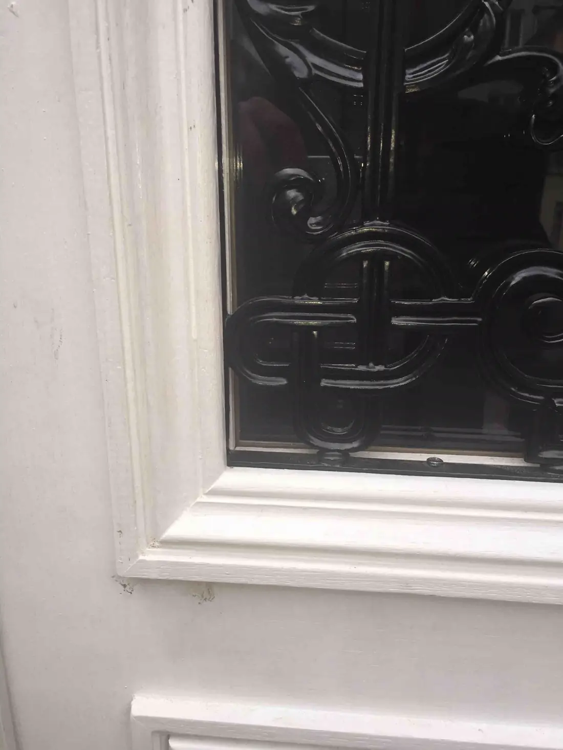 Détail d’une grille en fer forgé noire posée sur le vitrage d’une porte