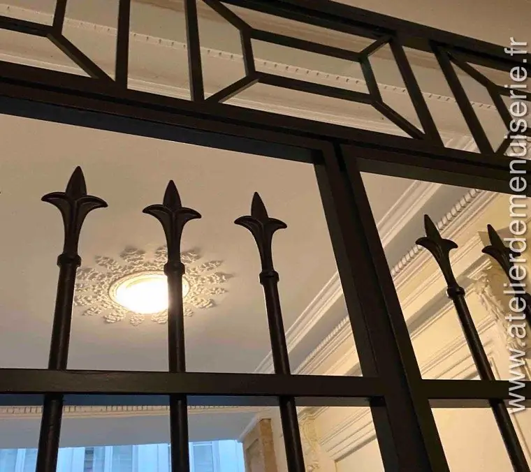 Grille de sas à fers de lance, vue en contre-plongée sous une rosace de plafond