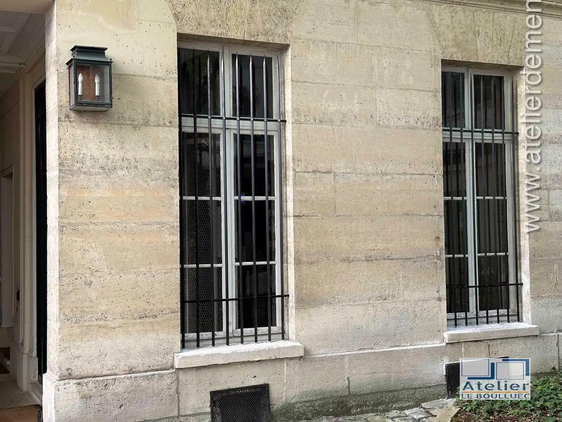Deux fenêtres équipées de grilles de défense sur une façade en pierre de taille