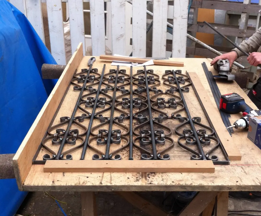Façonnage d’une grille à volutes serrée sur un établi, perceuse en main