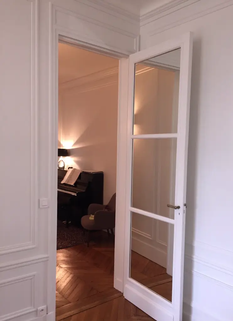 Porte intérieure vitrée blanche à petits bois moulurés, ouverte sur un parquet